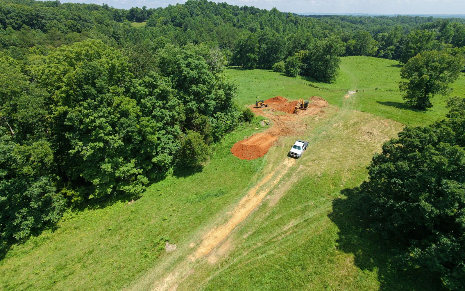 Aerial view of a PGS mini excavator and compact track loader digging a basement for a new home in open pasture near Hilham, Tennessee
