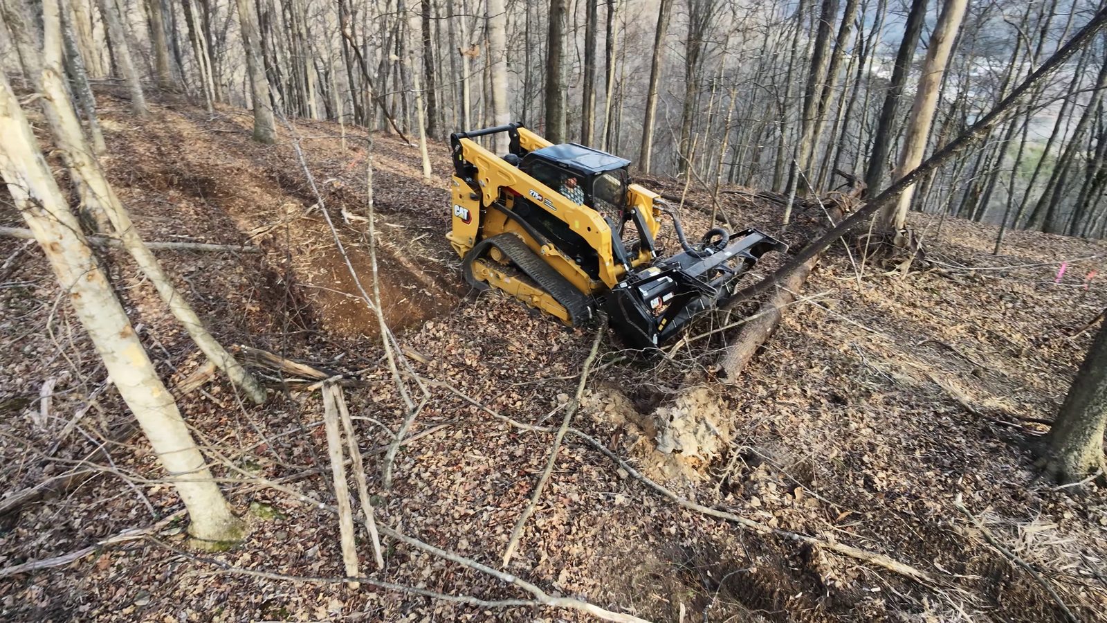 CAT compact track loader with mulcher on a steep wooded hillside