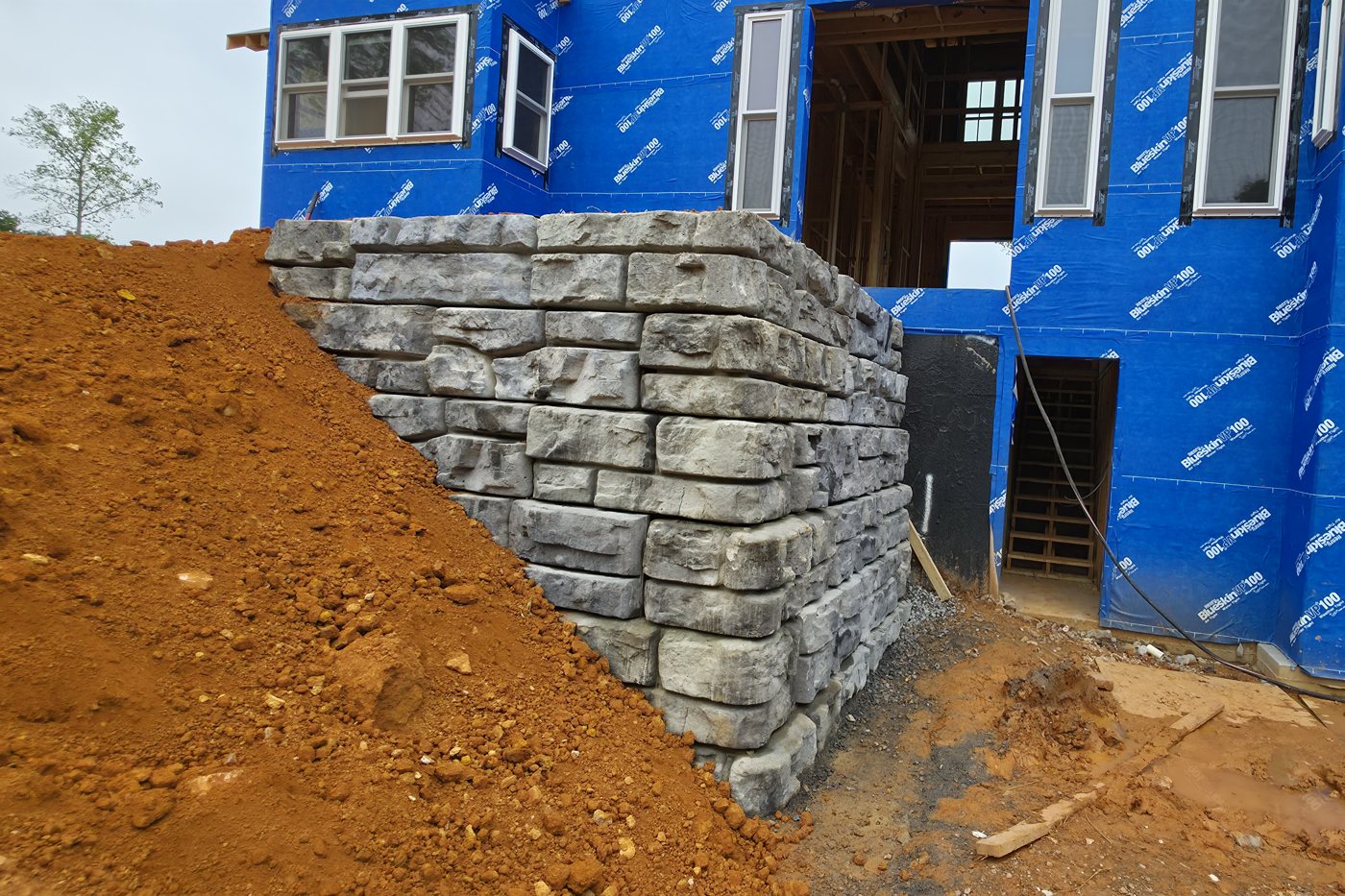 Finished Redi-Rock retaining wall seen straight on, dry and gray, with the new house behind it, Gainesboro TN