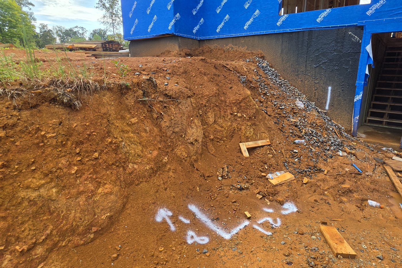 Raw red clay cut beside a walkout basement in Gainesboro with paint marks laying out the retaining wall and standing water at the low spot